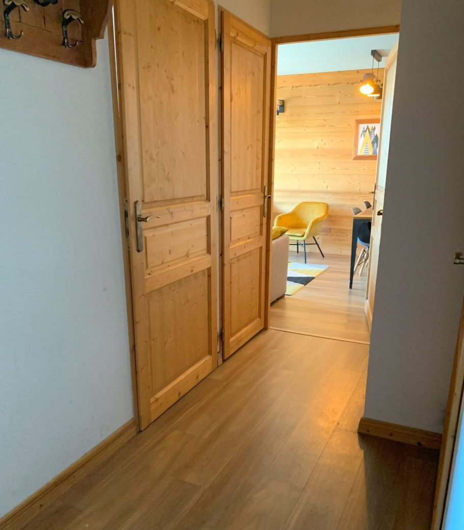 Couloir avec deux portes en bois et vue sur un salon éclairé.