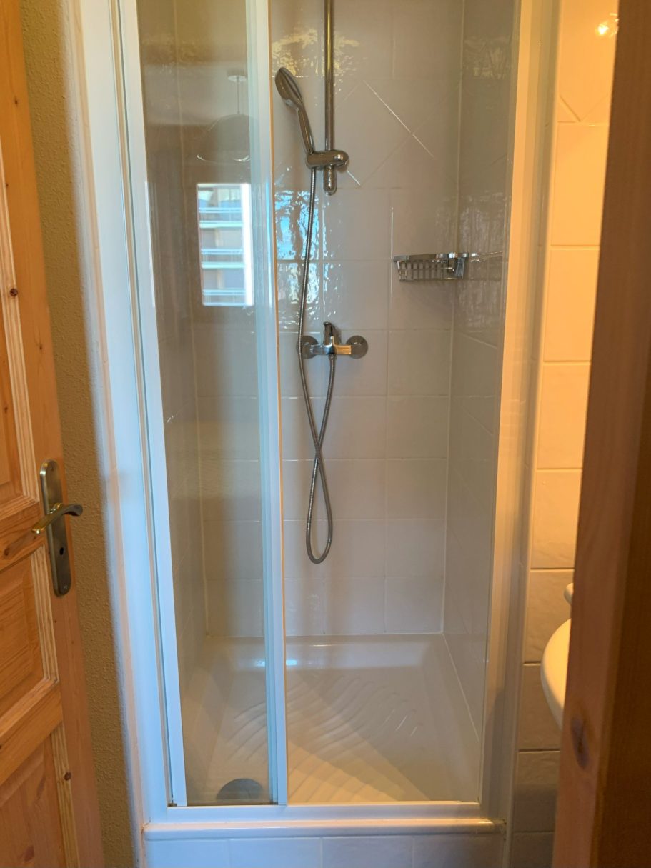 Douche avec parois en verre, robinetterie murale et sol carrelé.